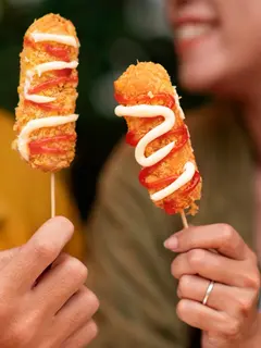 Dua orang sedang menunjukkan kuliner kekinian corndog sosis (Sumber: Freepik)