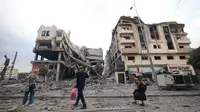 Warga Palestina membawa barang-barang pribadi berjalan melewati bangunan yang rusak parah setelah serangan udara Israel di distrik al-Rimal, Kota Gaza, pada 10 Oktober 2023. (Mahmud HAMS/AFP)