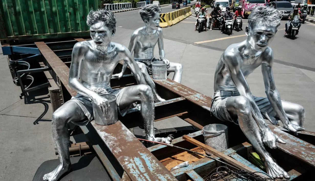 Foto nan diambil pada 7 April 2025 ini menunjukkan manusia silver Keris Munandar (kanan), saudaranya Ari Munandar (kiri), dan tetangganya Riyan Ahmad Fazriyansah menumpang di bagian belakang truk kontainer untuk mencapai persimpangan di Jakarta. (Yasuyoshi CHIBA/AFP)