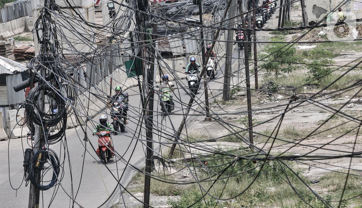Kendaraan melintas dekat instalasi kabel yang semrawut di Jalan Raya Bekasi, Cakung, Jakarta, Rabu (30/9/2020). Minimnya perawatan pascapembebasan lahan permukiman untuk proyek Tol Dalam Kota membuat jaringan kabel listrik di sepanjang jalan tersebut semrawut. (merdeka.com/Iqbal S. Nugroho)