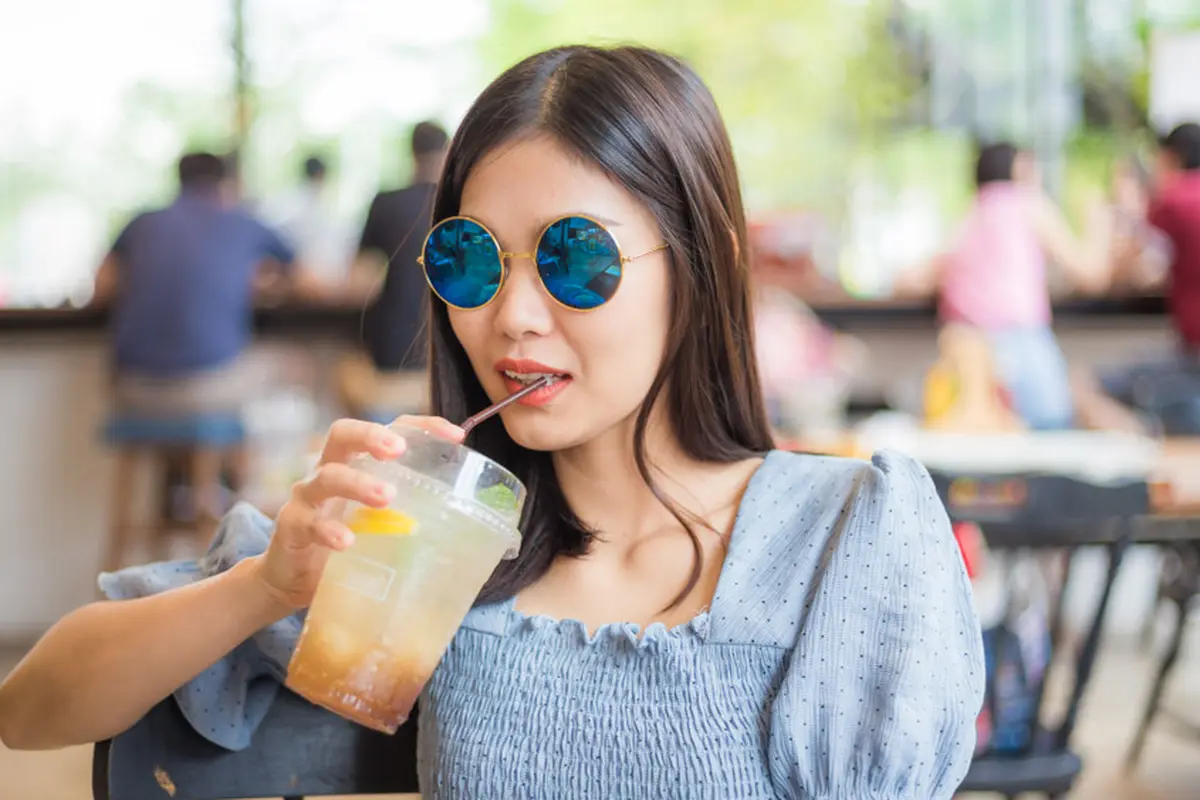 perempuan bahagia pakai kacamata minum di kafe
