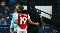 Manajer Arsenal, Mikel Arteta, merangkul gelandang timnya, Leandro Trossard, ketika meninggalkan lapangan saat babak pertama laga kontra Man City di Etihad Stadium, Minggu (22/9/2024) malam WIB. Leandro Trossard mendapatkan kartu merah pada akhir babak pertama. (Paul ELLIS / AFP)