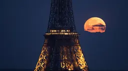 Foto yang diambil di Paris pada 23 April 2024 ini menunjukkan bulan purnama di bulan April, yang memiliki julukan pink moon atau bulan merah muda, terlihat di belakang Menara Eiffel. (Stefano RELLANDINI / AFP)