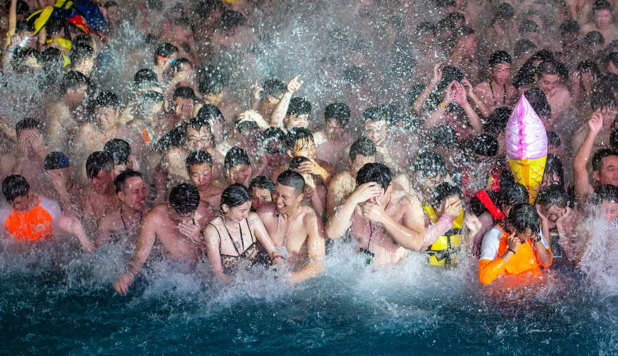 Pengunjung menyaksikan sebuah pertunjukkan sambil mendinginkan diri di kolam renang di Wuhan rovinsi Hubei, China pada 27 Juli 2019. Cuaca yang cukup panas membuat mereka berbondong-bondong menyesaki kolam renang. (Photo by - / AFP)