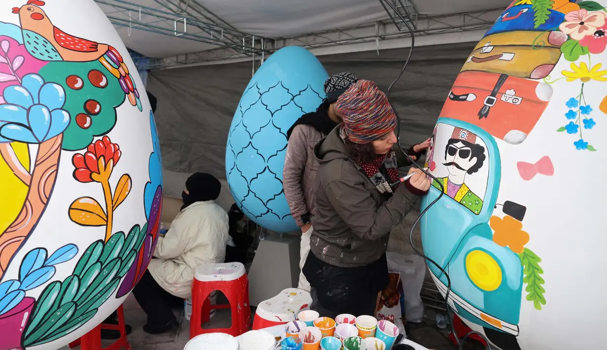 Para pelukis menghias telur-telur besar menjelang perayaan tahun baru Nowruz di Taman Mellat, Teheran, pada 27 Februari 2024. (ATTA KENARE/AFP)