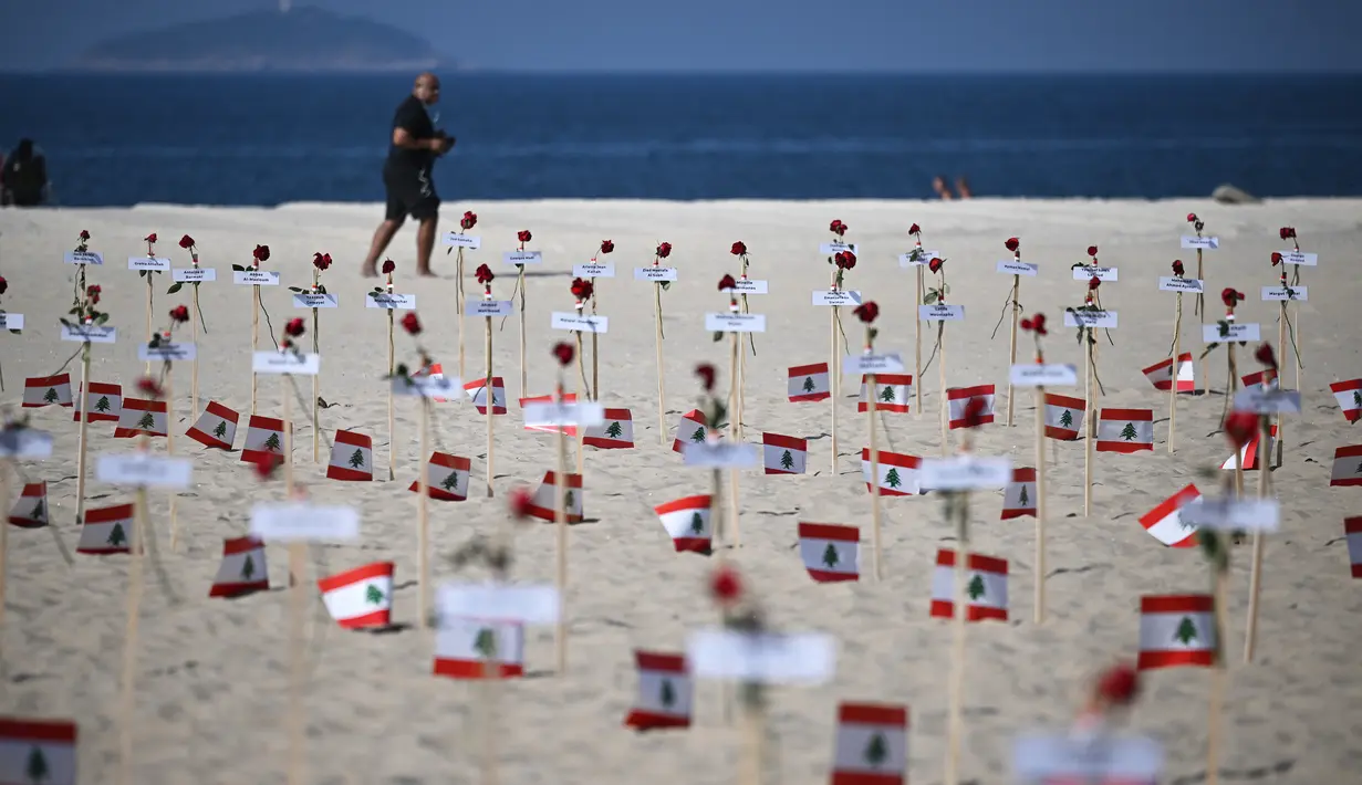 <p>Seorang pria berjalan melewati 245 mawar yang ditempatkan oleh LSM Rio da Paz beserta nama korban dan bendera Lebanon untuk memperingati 3 tahun sejak ledakan Beirut 2020 di Pantai Copacabana, Rio de Janeiro, Brasil, diambil pada 4 Agustus 2023. (AFP/Carl De Souza)</p>