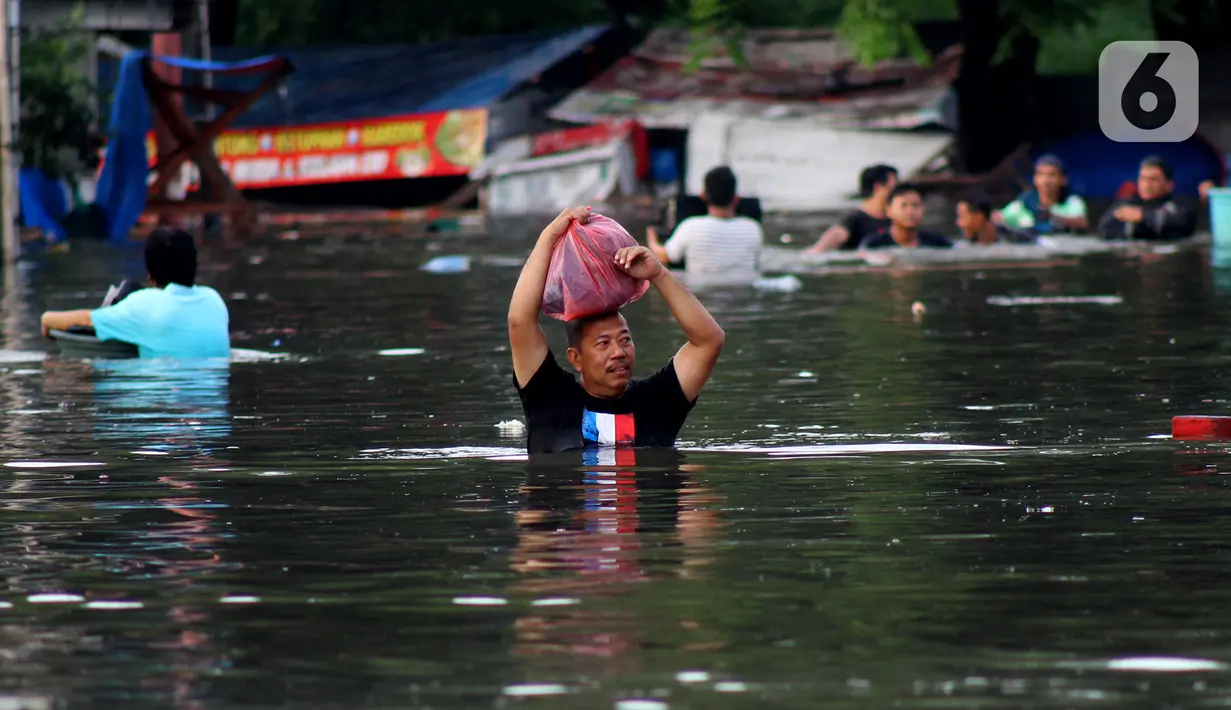 Warga melintasi banjir yang merendam perumahan Villa Mutiara Pluit, Tangerang, Banten, Senin (3/2/2020). Banjir disebabkan jebolnya tanggul sungai di sekitar kawasan tersebut. (merdeka.com/Magang/Muhammad Fayyadh)