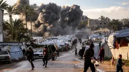 Serangan tersebut memicu kebakaran hebat yang menghanguskan sejumlah tenda pengungsi Palestina di lokasi kejadian. Tampak dalam foto, orang-orang berlarian berlatar kepulan asap hitam setelah serangan udara Israel menghantam sebuah lokasi dekat tenda-tenda penampungan pengungsi Palestina di Deir el-Balah, Jalur Gaza tengah pada 25 Maret 2026. (Eyad Baba/AFP)