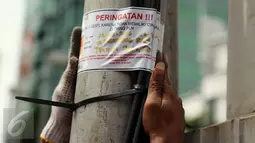 Petugas PLN menempelkan surat peringatan di tiang listrik kawasan Menteng Raya,Jakarta, (02/3). PLN akan menindak tegas pihak yang melakukan pelanggaran dengan memasang jaringan ilegal yang mengganggu pemandangan kota. (Liputan6.com/Faisal R Syam)