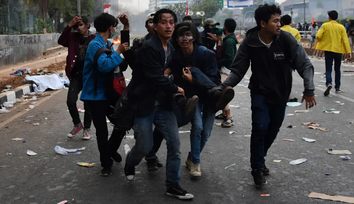 Sejumlah mahasiswa menggotong rekan mereka yang terluka saat demonstrasi menolak pengesahan RUU KUHP dan revisi UU KPK di depan Gedung DPR, Jakarta, Selasa (24/9/2019). Sejumlah mahasiswa tumbang setelah polisi menembakkan gas air mata untuk membubarkan demonstrasi. (ADEK BERRY/AFP)