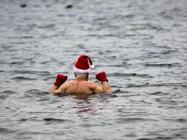 Anggota klub renang "Berliner Seehunde" (Berlin Seals) turun ke danau Orankesee sebagai bagian dari tradisi berenang pada Natal di Berlin, Jerman, Senin (25/12). Kegiatan ini salah satu tradisi di Berlin menyambut Natal setiap tahun. (AP/Markus Schreiber)