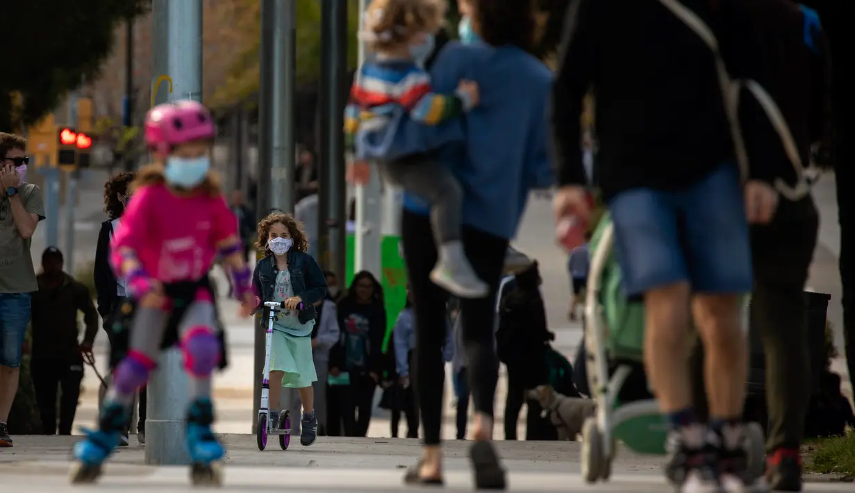 Keluarga dengan anak-anak mereka berjalan di sepanjang bulevar di Barcelona, Spanyol (26/4/2020). Dengan mulai lambatnya kenaikan angka kasus terjangkit membuat warga Spanyol optimis untuk bangkit kembali. (AP Photo/Emilio Morenatti)
