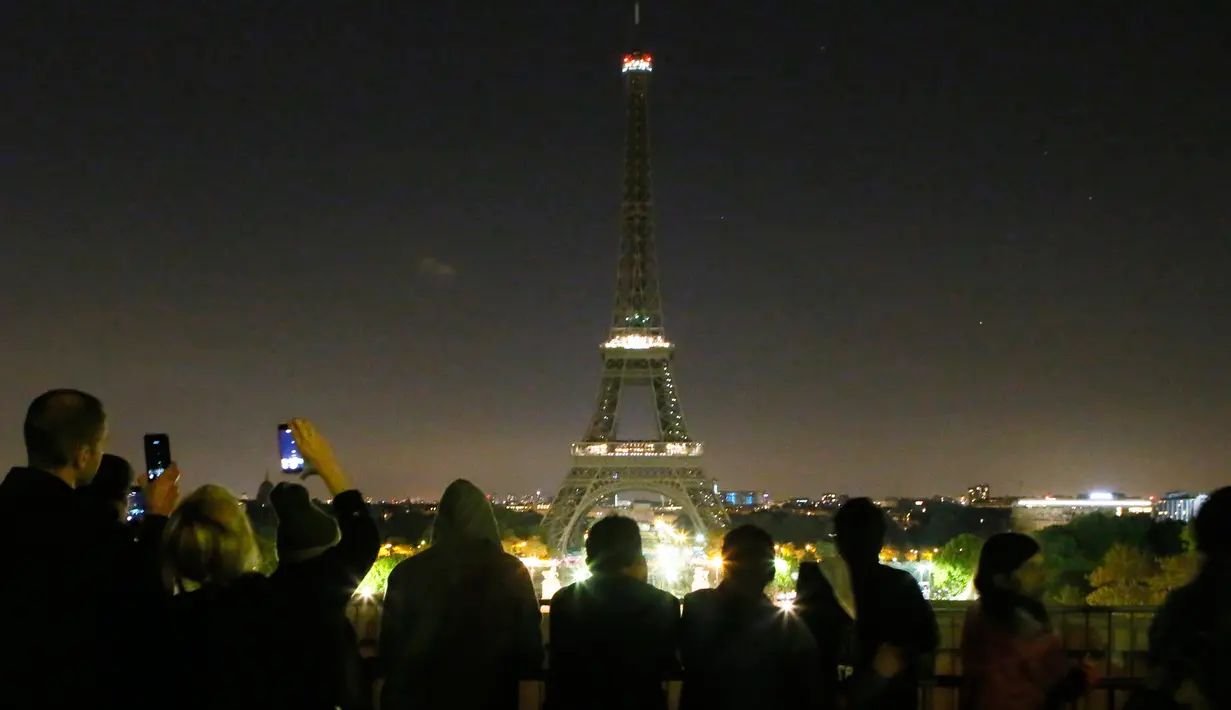 Pengunjung mengambil gambar saat pemadaman lampu Menara Eiffel di Paris, Rabu (24/5) dini hari. Hal tersebut dilakukan sebagai bentuk penghormatan dan duka cita atas serangan bom pada konser Ariana Grande di Manchester, Inggris. (AP Photo/Francois Mori)