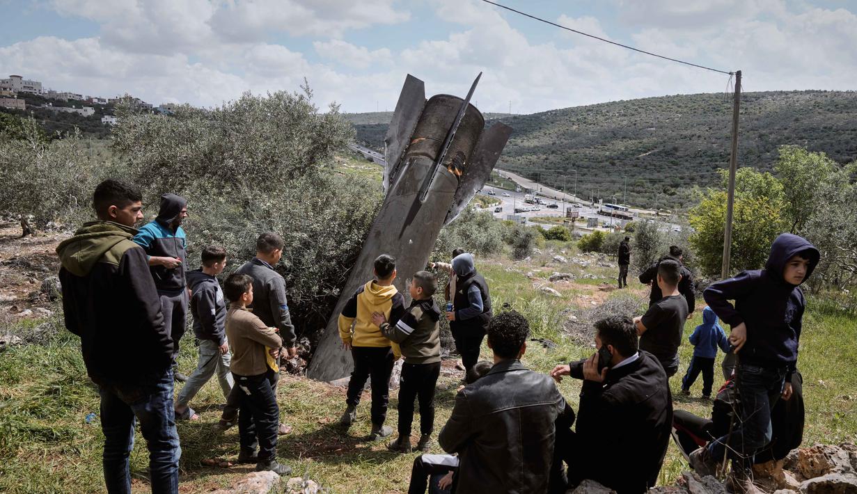 Penemuan ini merupakan dampak dari rentetan serangan rudal balistik yang diluncurkan Iran ke wilayah Israel dan sekitarnya. Tampak dalam foto, warga Palestina mengamati puing-puing rudal Iran yang jatuh di desa Kifl Haris, Tepi Barat, Selasa, 24 Maret 2026. (AP Photo/Majdi Mohammed)
