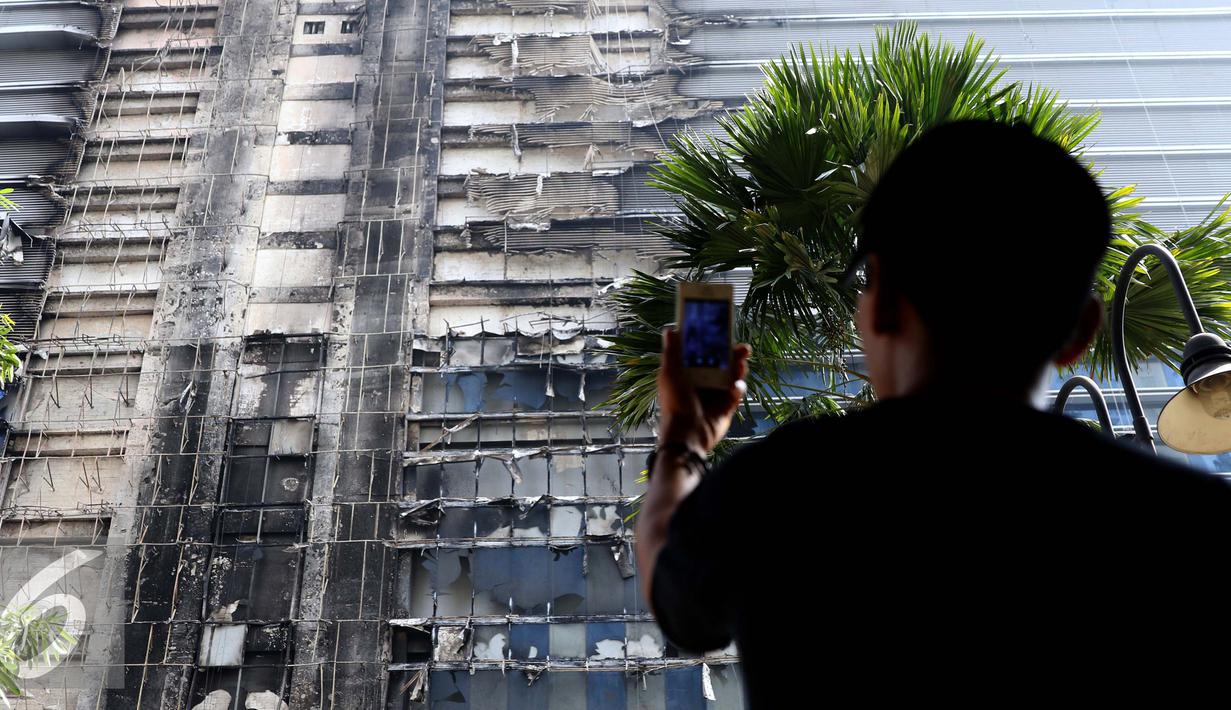 Seorang penghuni apartemen mengambil gambar Gedung Neo Soho pasca kebakaran di Tanjung Duren, Jakarta, Kamis (10/11). Kebakaran Gedung yang masih dalam tahap pembangunan itu terjadi Rabu (9/11) sekitar pukul 20.30. (Liputan6.com/Gempur M. Surya)