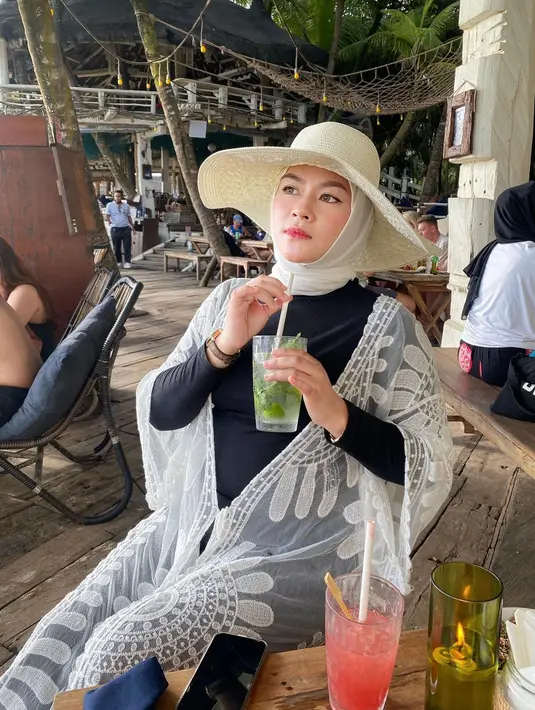 Begini gaya santai Yunita Lestari saat duduk di tepian pantai sambil menikmati minuman. Penampilannya semakin kece dengan mengenakan topi bundar. (FOTO: instagram.com/lee_yunita/)
