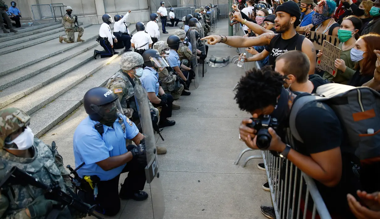 Polisi dan Garda Nasional Philadelphia berlutut saat pawai menyerukan keadilan atas kematian George Floyd di luar markas besar Kepolisian Philadelphia, Senin (1/6/2020). George Floyd tewas tak bisa bernafas karena tercekik lutut polisi saat ditangkap pada (25/5/2020) lalu. (AP/Matt Rourke)
