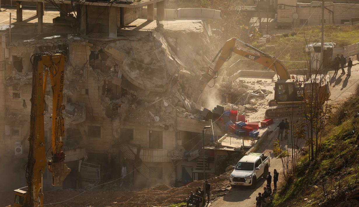 Beberapa buldoser dikerahkan untuk menghancurkan bangunan berisi 13 apartemen di lingkungan Wadi Qaddum, distrik Silwan, selatan Kota Tua Yerusalem. Tampak dalam foto, pasukan Israel berkumpul saat sebuah ekskavator merobohkan sebuah bangunan yang dibangun tanpa izin di lingkungan Wadi Qaddum, Yerusalem timur, pada Senin 22 Desember 2025. (Ahmad GHARABLI/AFP)