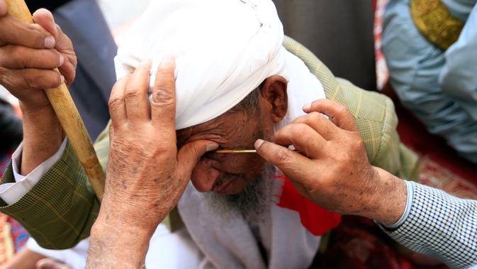 Seorang pria Yaman mengoleskan kosmetik tradisional kohl ke kelopak mata pria lain di Masjid Agung, kota tua Sanaa pada 9 mei 2019. Bagi muslim Yaman, pemakaian kohl diyakini mampu membersihkan dan melindungi mata dari penyakit ini sudah menjadi tradisi setiap bulan Ramadan. (MOHAMMED HUWAIS/AFP)