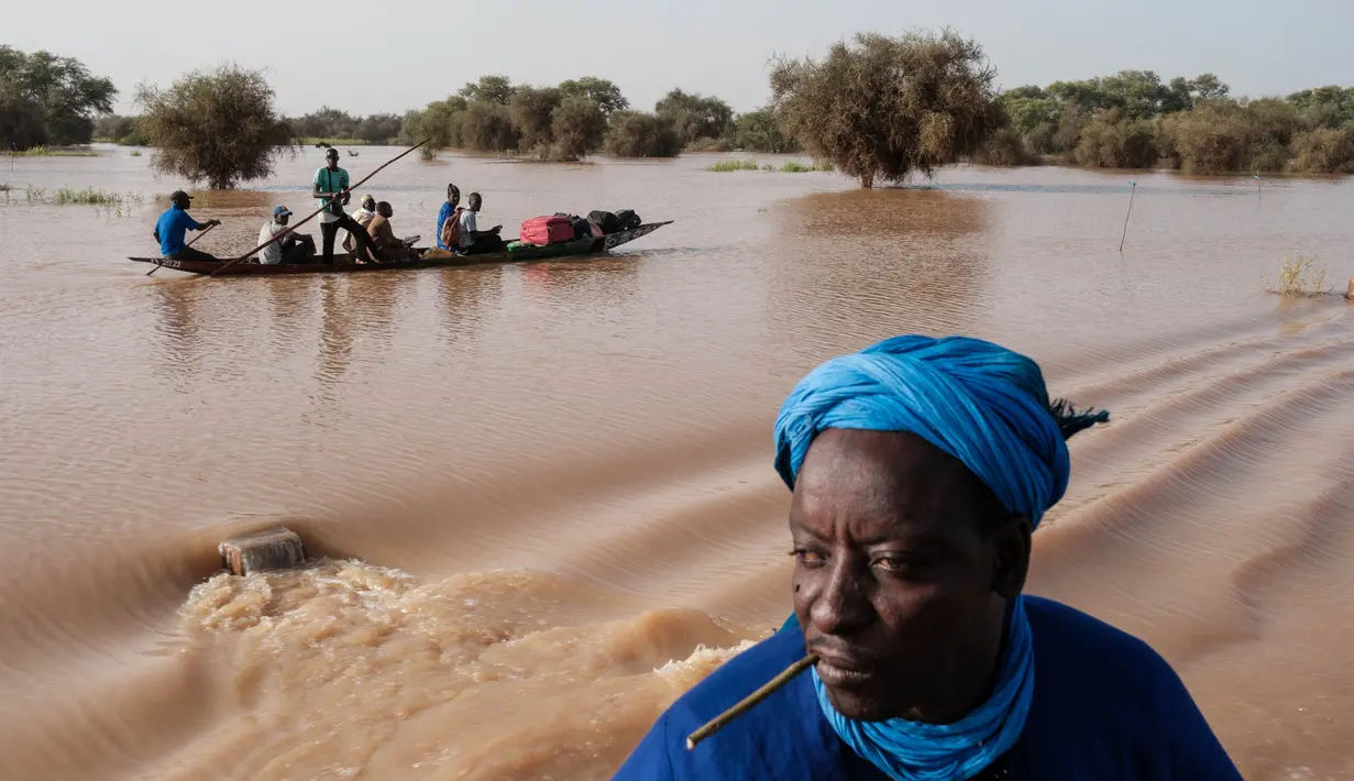 Orang-orang membawa barang-barang di atas kereta dorong di atas air banjir yang mengalir di jalan utama Odobere pada tanggal 22 Oktober 2024. (GUY PETERSON/AFP)