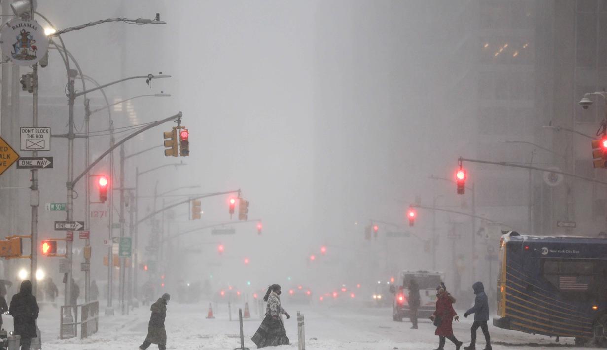Badai menyebabkan ribuan penerbangan dibatalkan hingga pemadaman listrik besar-besaran. Tampak dalam foto, orang-orang berjalan melintasi Sixth Avenue saat salju turun di distrik Manhattan, Kota New York, pada Minggu 25 Januari 2026. (CHARLY TRIBALLEAU/AFP)