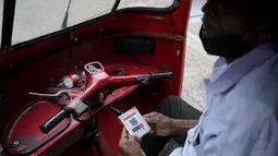 Seorang pengemudi bajaj menunggu untuk membeli bahan bakar dengan memegang kode QR di sebuah pompa bensin di Kolombo, Sri Lanka, Senin, 1 Agustus 2022.  Sri Lanka memperkenalkan distribusi bahan bakar menggunakan kode QR pada hari Senin sebagai bagian dari penerapan kuota mingguan untuk pengendara. (AP Photo/Eranga Jayawardena)