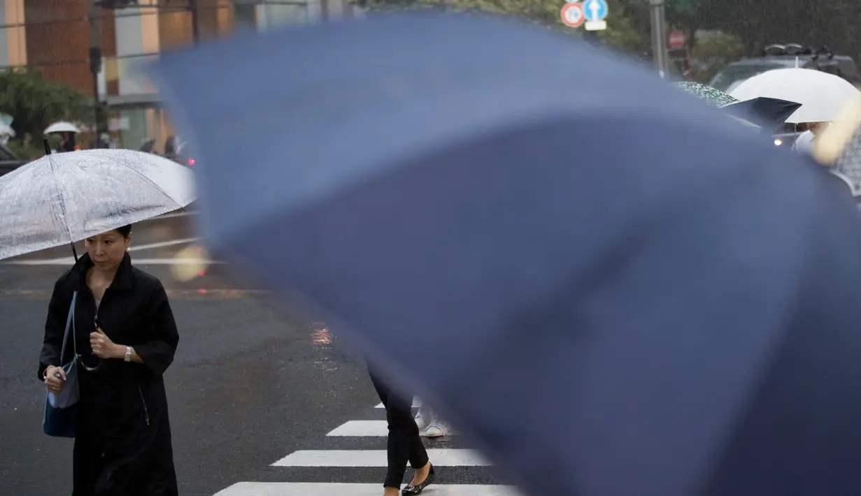Seorang wanita menggunakan payung berjalan saat hujan turun di Tokyo, Jepang (8/8). Topan kuat sedang mengarah ke Jepang pada 8 Agustus, mendorong badan cuaca untuk memperingatkan akan terjadi hujan lebat dan angin kencang. (AFP Photo/Behrouz)