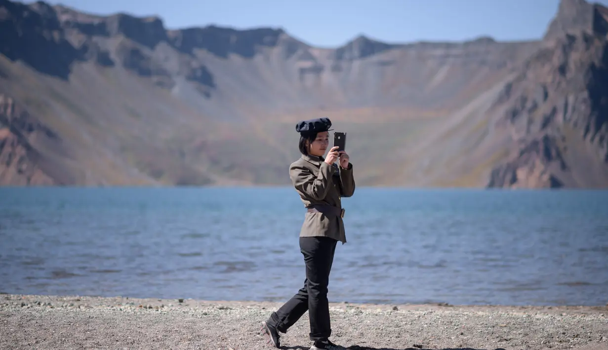 Gambar pada 11 September 2019 memperlihatkan siswa Korea Utara bermain ponsel di depan danau Chonji atau 'Heaven lake' saat mengunjungi kawasan Gunung Paektu di Samjiyon. 'Heaven lake' atau Danau surga ini ada di ketinggian 2.190 mdpl dan punya kedalaman 384 meter. (Photo by Ed JONES / AFP)
