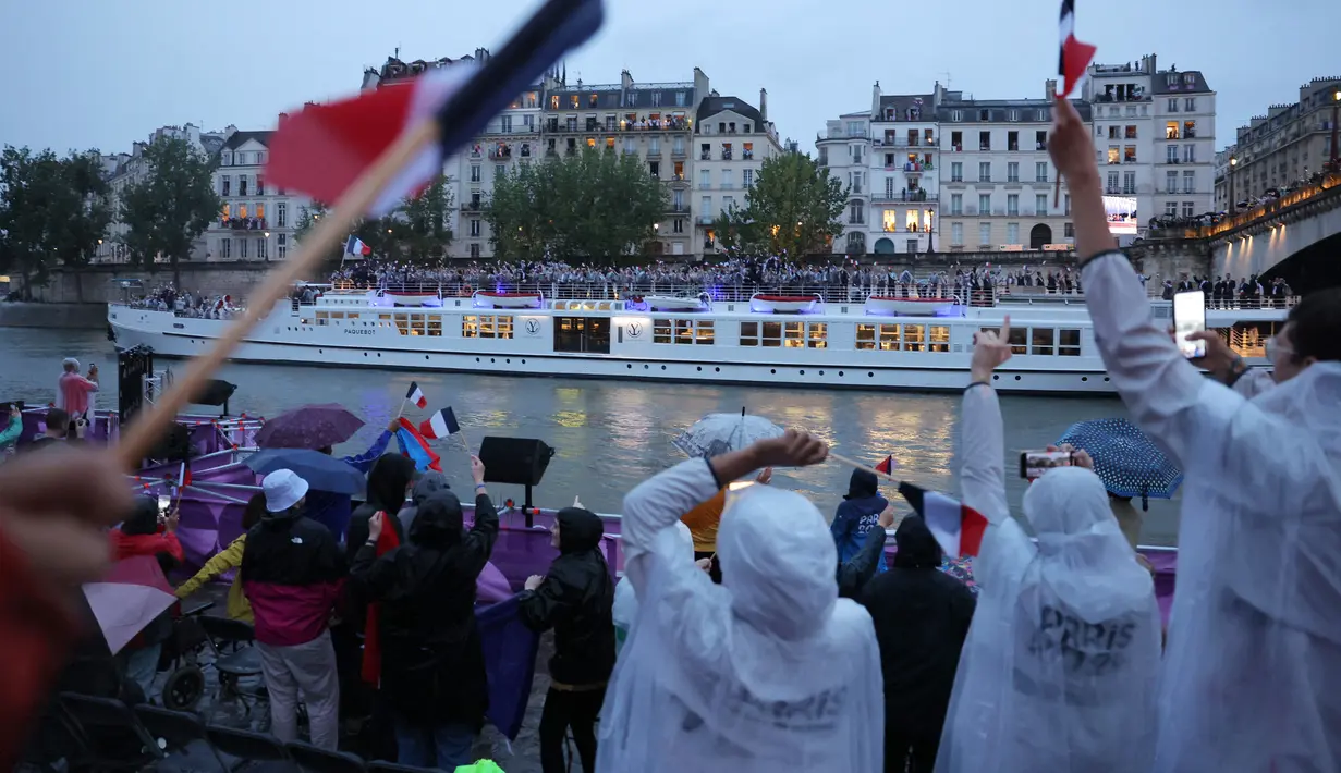 Mereka tetap berada di tempat dengan menggunakan payung serta jas hujan untuk menonton defile Olimpiade. (Ann Wang / POOL / AFP)