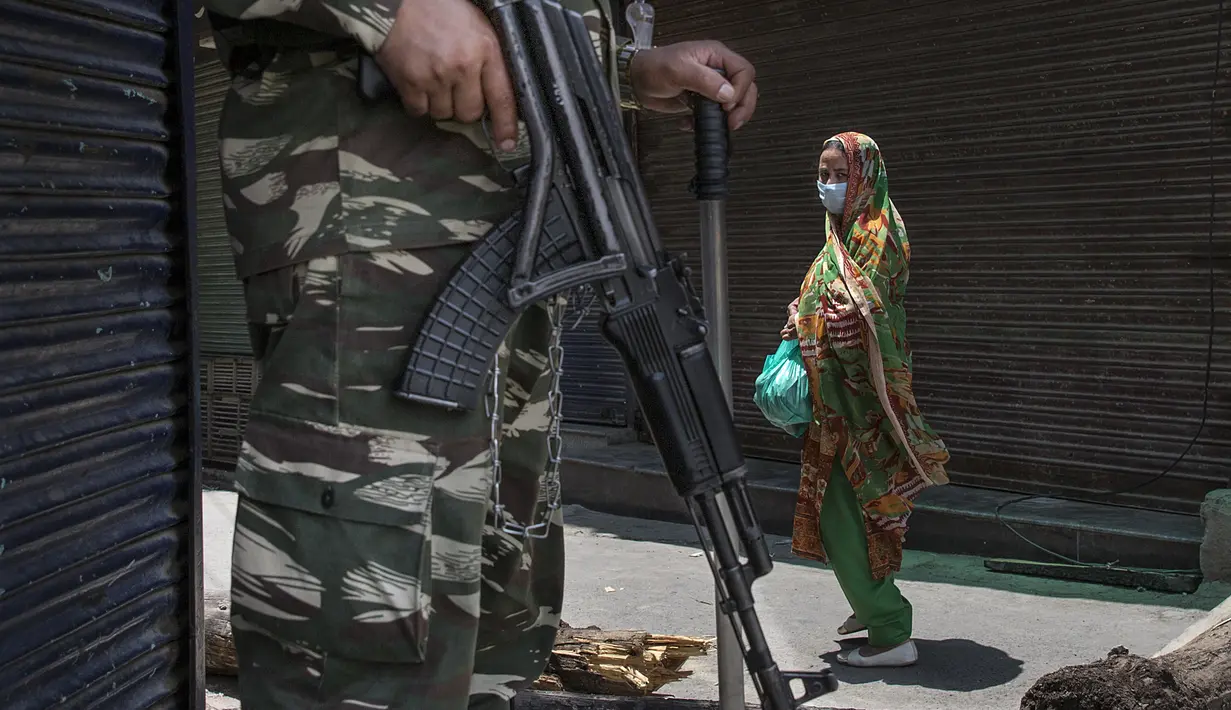 Seorang wanita berjalan melewati barikade yang dijaga tentara paramiliter India saat penerapan karantina wilayah (lockdown) guna membendung penyebaran pandemi COVID-19 di Kota Srinagar, ibu kota musim panas Kashmir yang dikuasai India (26/7/2020). (Xinhua/Javed Dar)
