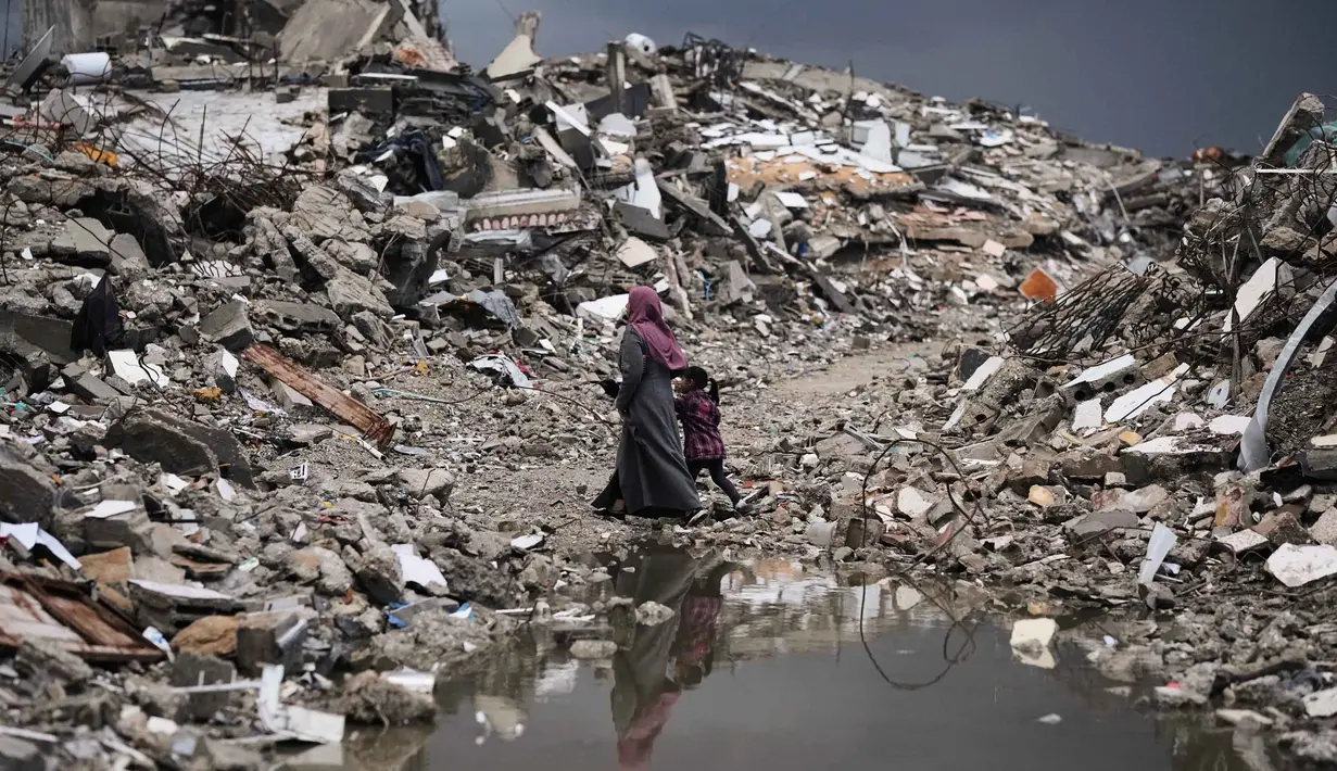 Diketahui, sebagian besar warga masih menempati tenda-tenda dan tempat penampungan sementara lainnya setelah perang antara Israel dan Hamas sejak Oktober 2023 silam. Tampak dalam foto, warga Palestina berjalan melewati reruntuhan di tengah cuaca buruk Kota Gaza, Kamis 11 Desember 2025. (AP Photo/Jehad Alshrafi)