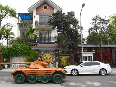 Truong Van Dao melewati sebuah rumah dengan tank kayu di daerah perumahan di provinsi Bac Ninh pada 28 Maret 2022. Seorang ayah di Vietnam telah menghabiskan ratusan jam dan menginvestasikan uangnya untuk mengubah mobil van tua menjadi tank kayu untuk putranya. (Nhac NGUYEN /AFP)