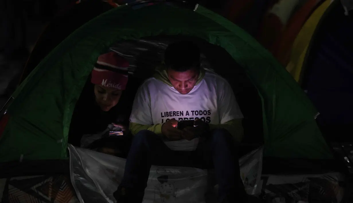 Sebagian keluarga tahanan memilih berkemah di luar penjara El Rodeo I di Guatire, Negara Bagian Miranda, sekitar 30 kilometer sebelah timur Caracas, Venezuela. Tampak dalam foto, seorang pria menggunakan telepon seluler di atas tenda yang didirikan oleh kerabat tahanan politik di luar penjara El Rodeo I di Guatire, Negara Bagian Miranda, sekitar 30 kilometer sebelah timur Caracas, Venezuela, pada 12 Januari 2026. (Pedro MATTEY/AFP)