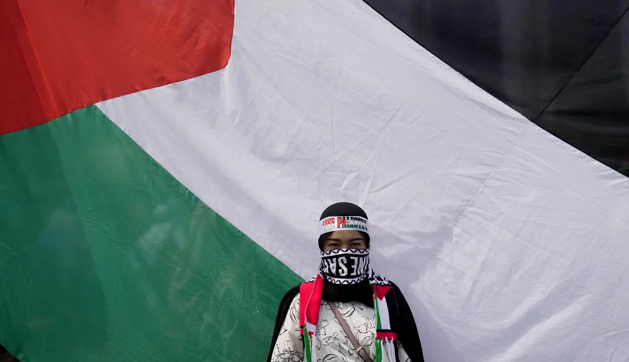 Seorang perempuan berdiri di depan bendera besar Palestina saat aksi bela Palestina, di Monumen Nasional atau Monas, Jakarta Pusat, Minggu (5/11/2023). (AP Photo/Dita Alangkara)