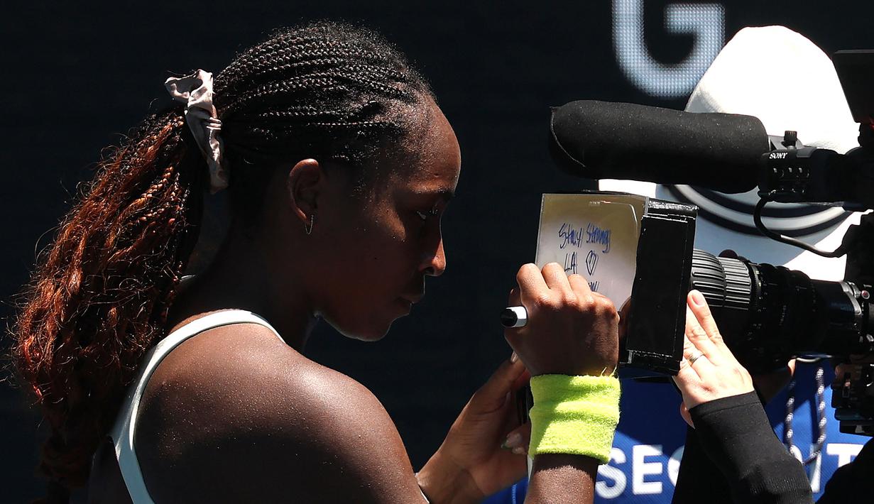 Petenis Amerika Serikat, Coco Gauff menuliskan pesan untuk korban kebakaran dan pemadam kebakaran di Los Angeles, Amerika setelah menang atas kompatriotnya, Sofia Kenin pada hari kedua Australia Open 2025 di Melbourne, Australia, Senin (13/01/2025). (AFP/David Gray)