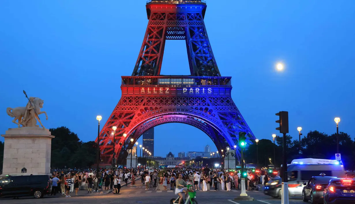 Orang-orang berjalan di bawah Menara Eiffel yang diterangi cahaya warna-warna khas, dengan pesan bertuliskan "Allez Paris" ("Ayo, Paris"), pada malam menjelang pertandingan final Liga Champions 2025/2026 antara Paris Saint-Germain (PSG) dan Arsenal, Kamis 29 Mei 2026. (Ludovic MARIN/AFP)