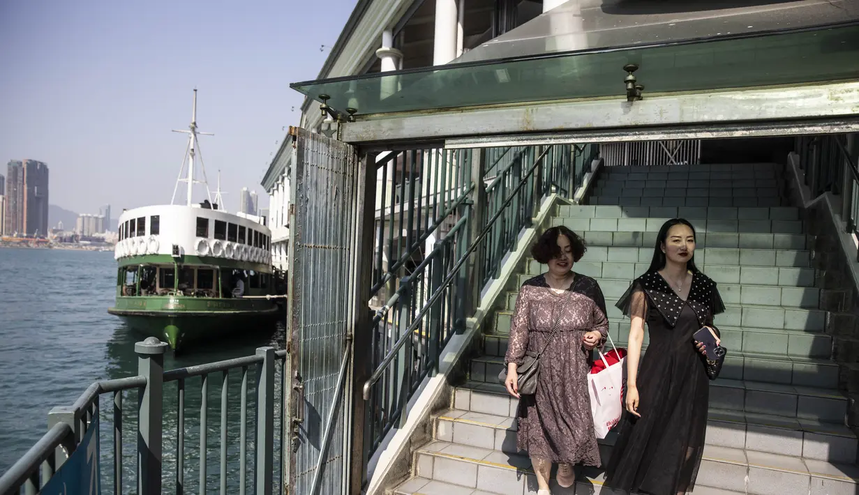 Dua wanita turun dari Star Ferry di Hong Kong (1/3/2023). Hong Kong menjadi salah satu tempat terakhir di dunia yang masih menerapkan aturan masker. (AFP/Isaac Lawrence)