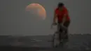 Gerhana bulan terlihat di belakang pengendara sepeda saat blood moon pertama tahun ini di Irwindale, California, Amerika Serikat, Minggu (15/5/2022). (AP Photo/Ringo H.W. Chiu)
