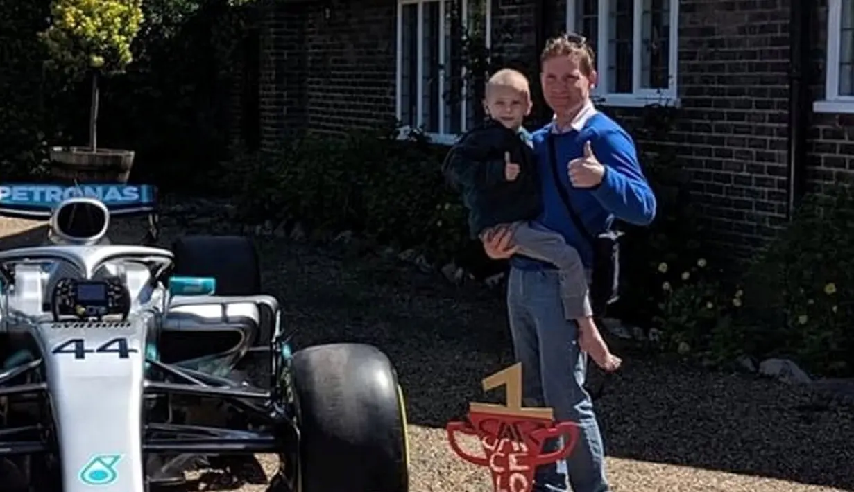 Bocah penderita kanker tulang langka Harry Shaw digendong ayahnya melihat mobil F1 yang dia terima dari Lewis Hamilton di Redhill, Surrey, Inggris, 13 Mei 2019. Hamilton menghadiahi mobil Mercedes yang dipakai dalam balapan F1 kepada bocah berusia lima tahun tersebut. (James Shaw/via REUTERS)
