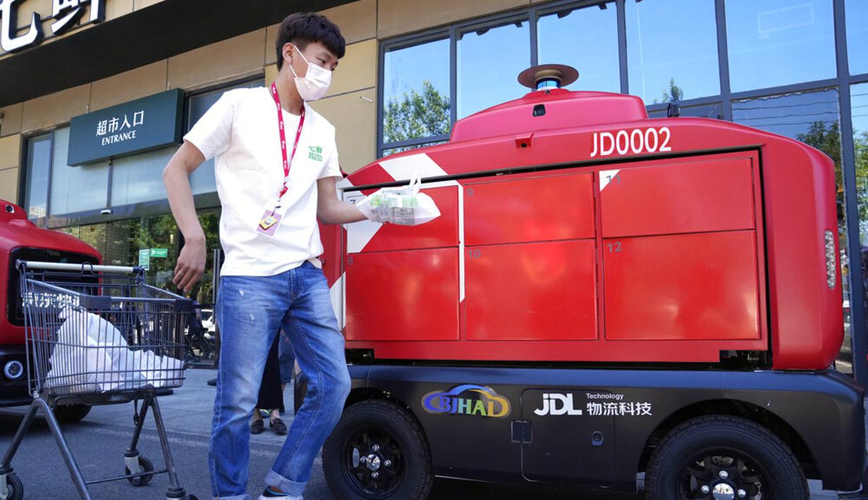 Seorang pekerja bersiap untuk memuat pengiriman ke kendaraan pengiriman otonom dari JD.com di jalanan Beijing, China, Jumat (28/5/2021). Raksasa e-commerce China JD.com meningkatkan operasi kendaraan pengiriman tak berawak. (AP Photo/Ng Han Guan)