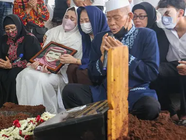 Nia Zulkarnaen, putri aktris senior Mieke Wijaya, menangis sambil memegang foto sang ibunda saat prosesi pemakaman di TPU Tanah Kusir, Jakarta, Rabu (4/5/2022). Mieke Wijaya meninggal dunia pada Selasa, 3 Mei 2022 di Jakarta. Ia meninggal dunia pada usia 82 tahun. (Liputan6.com/Herman Zakharia)