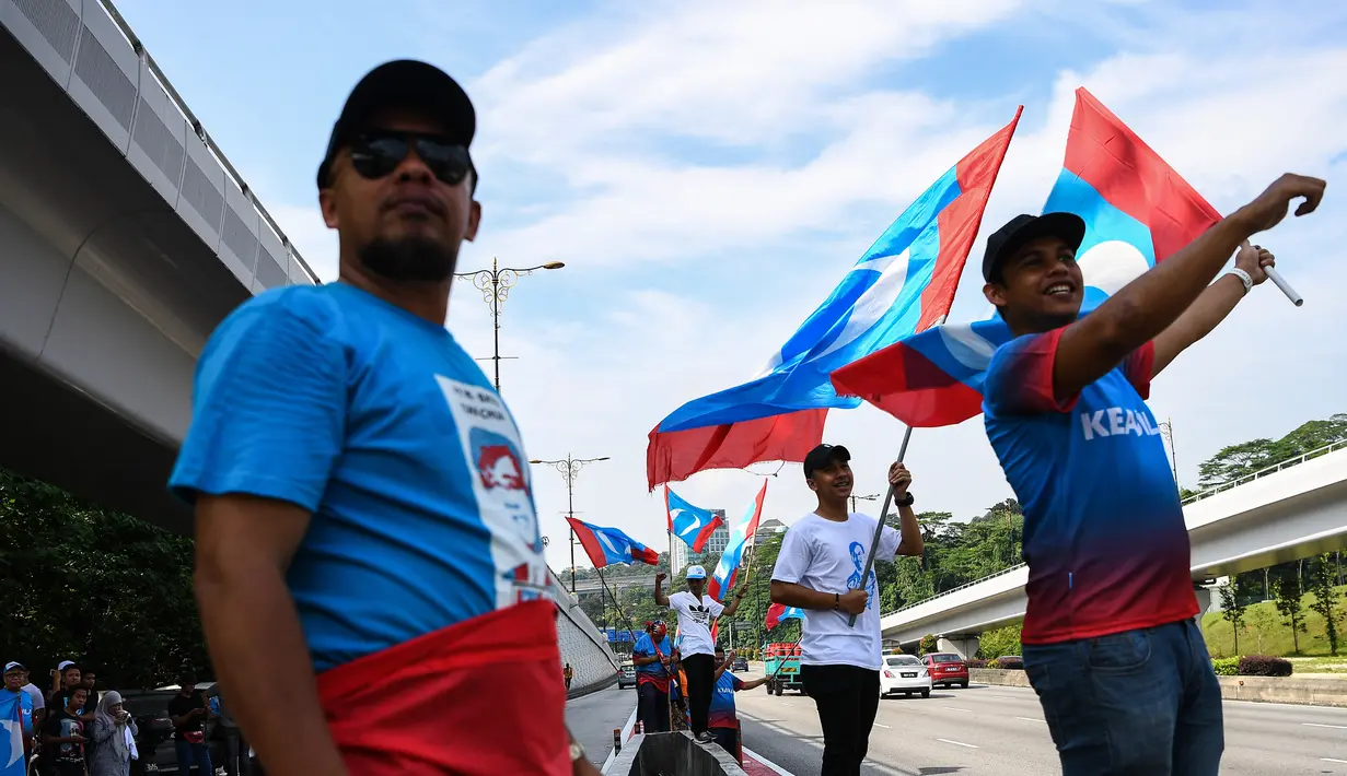 Warga melambaikan bendera Pakatan Harapan di sepanjang jalan menuju Istana Negara menjelang pelantikan Mahathir Mohamad sebagai PM Malaysia di Kuala Lumpur, Kamis (10/5). Mahathir akan menjadi perdana menteri ketujuh Negeri Jiran. (AFP/Manan VATSYAYANA)