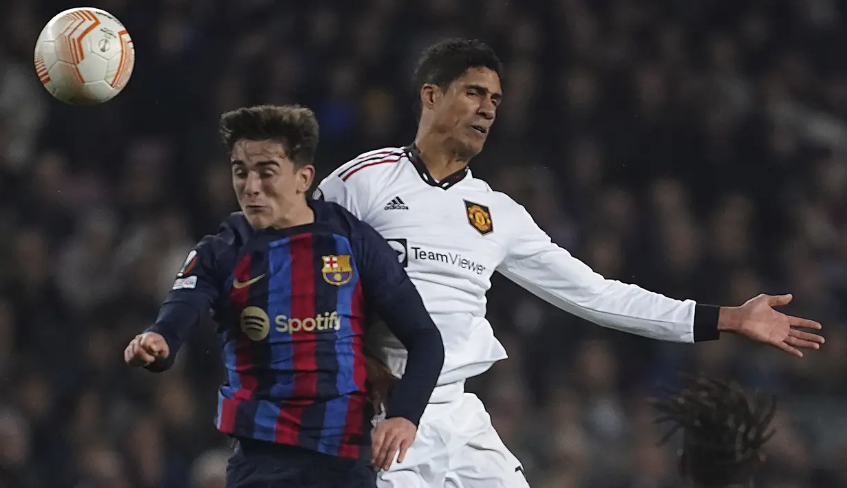 Gelandang Barcelona Gavi dan bek Raphael Varane Manchester United (MU) menyundul bola saat bersaing pada leg pertama play-off babak gugur Liga Europa 2022/2023 di Camp Nou, Jumat (17/2/2023) WIB. Barcelona mencetak gol pembuka lewat sundulan Marcos Alonso (50') dan gol penutup di pertandingan ini via Raphinha (76').  (AP Photo/Joan Monfort)