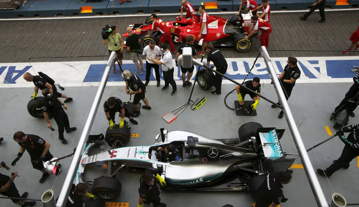 Mekanik mendorong mobil Ferrari yang digunakan Sebastian Vettel disamping mobil Lewis Hamilton di pit lane di Sirkuit Marina Bay jelang sesi latihan Grand Prix Singapura F1 (18/9/2015). (REUTERS/Edgar Su)