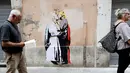 Pejalan kaki melewati mural Presiden AS, Donald Trump dan Paus Francis berciuman di sebuah dinding di Roma, Kamis (11/5). Sebuah keterangan terdapat di sisi lain dari mural yang bertuliskan, "The Good Forgives the Evil." (AP Photo/Alessandra Tarantino)