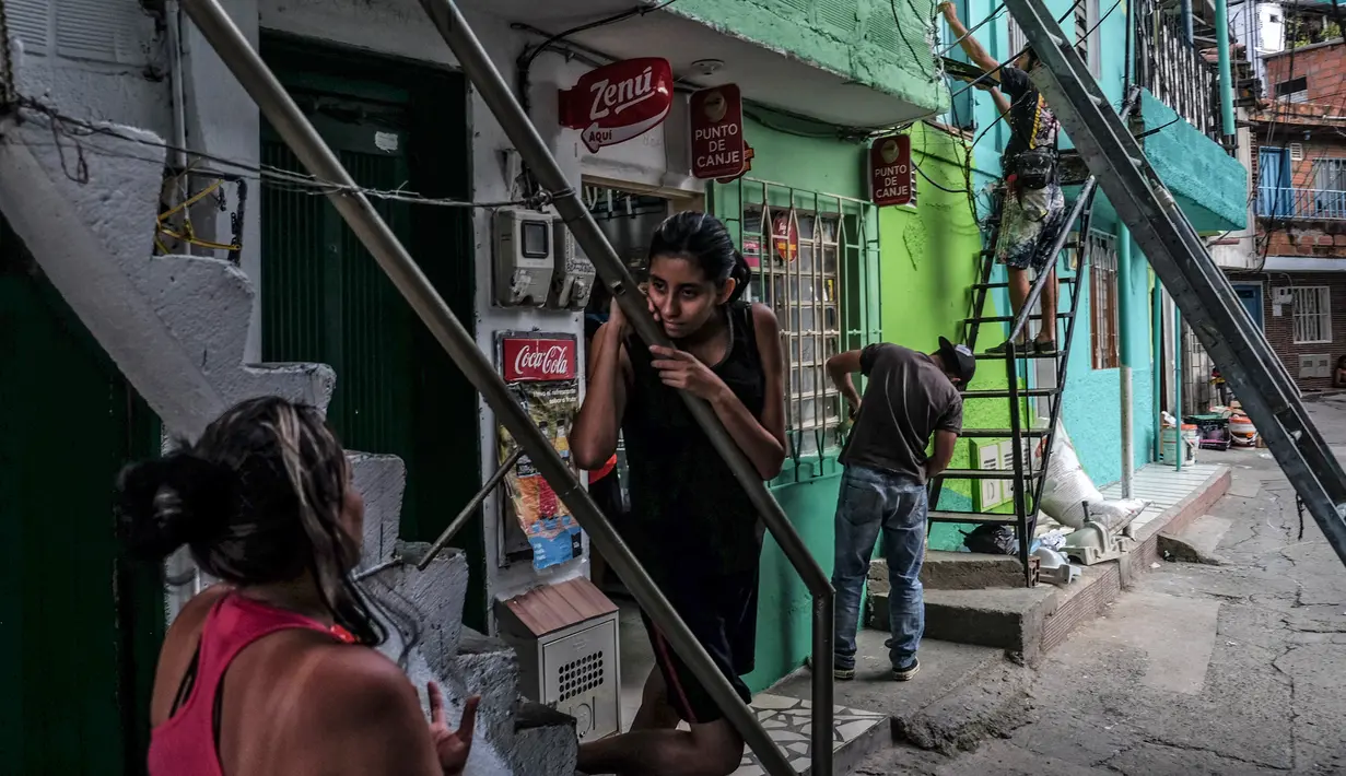 Seniman Prancis, Tarik Bouanani (kanan) melukis dinding di kawasan kumuh El Pesebre, pinggiran Medellin, Kolombia, 19 Juni 2017. Tarik melukis 230 rumah di kawasan itu sebagai bagian dari proyek seninya membentuk mural raksasa. (JOAQUIN SARMIENTO/AFP)