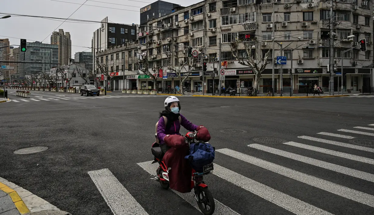 Seorang wanita mengendarai skuter di jalan yang sepi di distrik Yangpu, di Shanghai (28/3/2022). Jutaan orang di pusat keuangan China dikurung di rumah mereka pada Maret 28 ketika bagian timur Shanghai dikunci untuk mengekang wabah Covid terbesar di negara itu. (AFP/Hector Retamal)