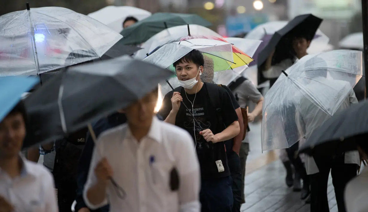 Seorang pria menggunakan payung berjalan saat hujan turun di Tokyo, Jepang (8/8). Sejumlah maskapai membatalkan penerbangan akibat cuaca yang kurang mendukung. (AFP Photo/Behrouz)