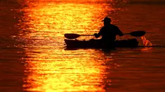 Seorang pria melintasi pantulan matahari terbenam saat berperahu di Shawnee Mission Lake, Shawnee, Kansas, Amerika Serikat, Jumat (9/10/2020). Matahari terbenam terus lebih cerah dari biasanya karena asap dari kebakaran hutan barat terus melayang di seluruh negeri. (AP Photo/Charlie Riedel)