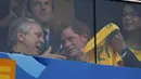 Dari balik kaca pelindung, Pangeran Harry terlihat memamerkan kaos Timnas Brasil kepada salah satu penonton yang ikut menyaksikan laga Brasil vs Kamerun di Stadion Nasional Brasil, (24/6/2014). (REUTERS/Ueslei Marcelino)